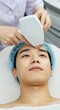 © soojin - A man lying on a dermatologist's bed receiving skin care using a beauty device.