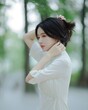 © Hailong - A young woman adjusting her hair in a serene outdoor setting.