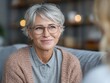 © Thananchakorn.A - Close-up of smiling senior woman with short gray hair wearing glasses and casual sweater in warm indoor setting