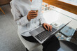 Businesswoman sitting and using laptop while holding takeaway coffee cup, working remotely in modern office space