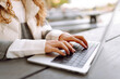 Portrait of a young woman in glasses sitting at a wooden table with a laptop in an autumn park. Nice female freelancer enjoying fresh air and working with a laptop. Remote work concept, weekend.