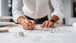 © tawat - A dedicated male architect meticulously drafting a detailed building plan on a large blueprint using professional drawing tools on his wooden desk in a well lit modern office
