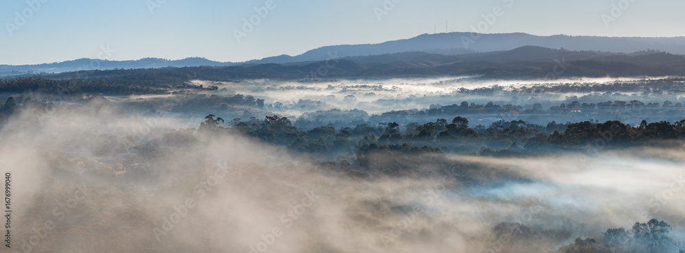 Aerial panorama of layers of fog lying in a valley of bushland below a ...
