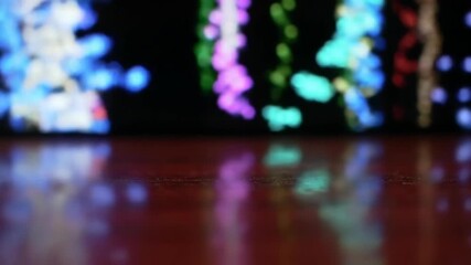 Abstract colorful light bokeh reflections on dark wood surface against black background.