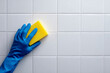 © heerim studio - Cleaning white tiled surface with blue gloved hand holding yellow sponge for sparkling results.