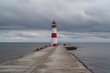 © ahmad - A red  white lighthouse stands at the end of a concrete pier under an overcast sky