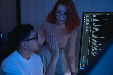 Two software developers collaborating at night, focusing on code review and debugging process on a computer screen, representing teamwork, innovation, and modern software development workflow.