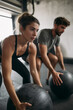 © Vitali - A pair of friends engaging in functional strength exercises using medicine balls at a minimalist fitness studio.