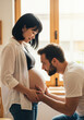 © Vasiliy - Pregnant asian woman with partner at home touching belly in natural light. Multicultural maternity moment for diverse family planning service documentation