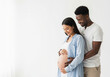 © Vasiliy - Multiracial pregnant couple embracing with hands on belly in studio portrait. Maternity session for family announcements and pregnancy milestone documentation