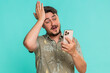 © Andrii Iemelianenko - Middle-aged man scrolls smartphone casually, then suddenly hits forehead with palm realizing he forgot something important. Young adult guy isolated on blue background showing memory lapse and urgency