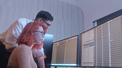 Two developer or programmer colleagues collaborating on programming and data analysis using monitors. They discuss code review system logs and share ideas in a modern office. Teamwork and technology.