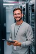 © Віталій Б. - A young man with glasses stands confidently in a data center, holding a tablet. He is surrounded by rows of server racks, showcasing a modern technology environment