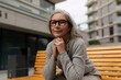 © Ivan Traimak - Senior woman enjoys a moment of reflection on a bench in a modern urban setting during a cloudy afternoon