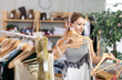 © JackF - Near clothes rack, girl buys tank top, chooses clothes. Discount season, promotional offers. Woman of fashion near showcase chooses summer clothes, examines goods