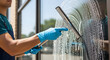 © delila - Professional worker in blue gloves performing window cleaning with a squeegee on a commercial glass surface