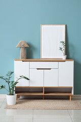 Poster - chest of drawers with lamp, blank frame and plants near green wall in room