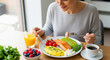 © ProArt Studios - A happy woman enjoys a nutritious and delicious healthy breakfast, featuring salmon, omelet, avocado, fresh berries, and coffee, by a sunlit window.