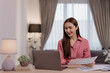 © Tj - Young Asian business woman attending online conference meeting, discussing with colleagues remotely via video call on laptop computer, holding financial document, working from home