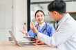 © PRIME STOCK LAB - Young female nurse and male doctor discussing patient chart at table with laptop and coffee, collaborative medical consultation conveying focused caring communication and teamwork