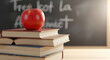 © K Media - A vibrant red apple sits atop a stack of hardcover textbooks on a wooden desk, a classic symbol of education and learning with a softly blurred classroom chalkboard in the background