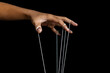 © Dadan - male puppeteer hand with strings isolated on black background. manipulation or controlling concept