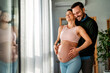 © NDABCREATIVITY - Man in love hugs his pregnant wife, they are waiting together for the baby's arrival. Love, family
