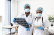 © sofiko14 - Two African American surgeons wearing masks in medical consultation, reviewing patient scans, collaborating in hospital. Their focus emphasizes teamwork and healthcare expertise