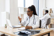 © sofiko14 - Young adult African American female doctor holding pill bottle, writing prescription, working in office