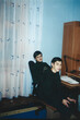 © Masson - Two teenagers sitting at a table with an old desktop computer in a Ukrainian home room, early 2000s analog photography with muted colors