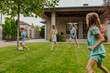 © Westend61 - Family playing football together on grassy lawn outside home in summer