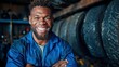 © Dulemegapixel - An engaging portrait of a smiling mechanic showcasing confidence and professionalism while surrounded by tires in a dynamic workshop environment filled with energy.