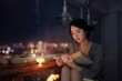 © Shuguang - Woman reading a book by the window at night with city lights in the background.