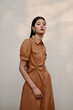 © Shuguang - Modern woman in brown dress standing against a simple background.