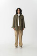 © Shuguang - Casual male model in olive green jacket and beige cargo pants, standing in minimal studio setting.