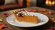 © Hamza - A slice of pumpkin pie decorated with a spiderweb design on a plate, surrounded by autumn leaves for a Halloween treat