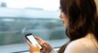 © Desg man - Young woman using her smartphone while traveling by train, looking out the window at the blurred scenery passing by