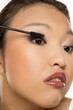 © vladimirfloyd - Closeup portrait of a young Asian woman applying mascara.