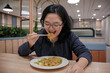 © Daniel Pawer - Happy woman enjoys stir fried vermicelli noodles with chopsticks in a cozy modern restaurant. The scene captures joyful dining, Asian cuisine.