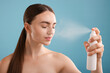 © New Africa - Beautiful woman spraying thermal water onto her face on light blue background