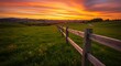 © GlambGarb - Vibrant sunset over a green meadow with a rustic wooden fence