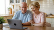 © Creative Garage - Senior couple smiling while looking at a laptop in a bright kitchen setting at home together