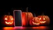 © mizan - Jack-o-Lantern pumpkins and a smartphone with neon lights on black background