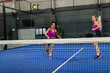 © Wavebreak Media - Diverse female padel partners playing on blue court in sports hall swinging rackets at ball