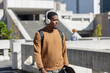 © Wavebreak Media - African american man walking in plaza wearing headphones, necklace, carrying skateboard backpack