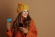 © Alliance - A smiling woman in warm autumn apparel holds a smartphone and credit card, looking thoughtfully to the side, suggesting she is planning or considering online purchases.