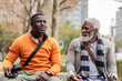 © Wavebreak Media - African american male friends sitting on park bench in city square using smartphone with headphones