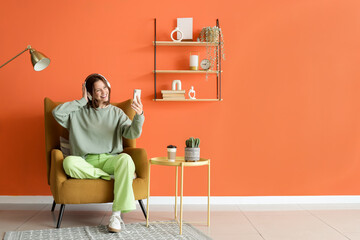 Poster - young woman with headphones and mobile phone sitting in armchair at home