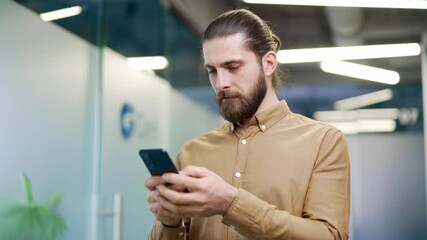 Businessman is using browsing mobile phone while standing workplace in a modern business office. Handsome entrepreneur is chatting online with client or reading writing message on smartphone. Close up