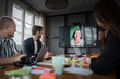 © Johnér - Business professionals discussing with female colleague on video call through television set in office meeting room